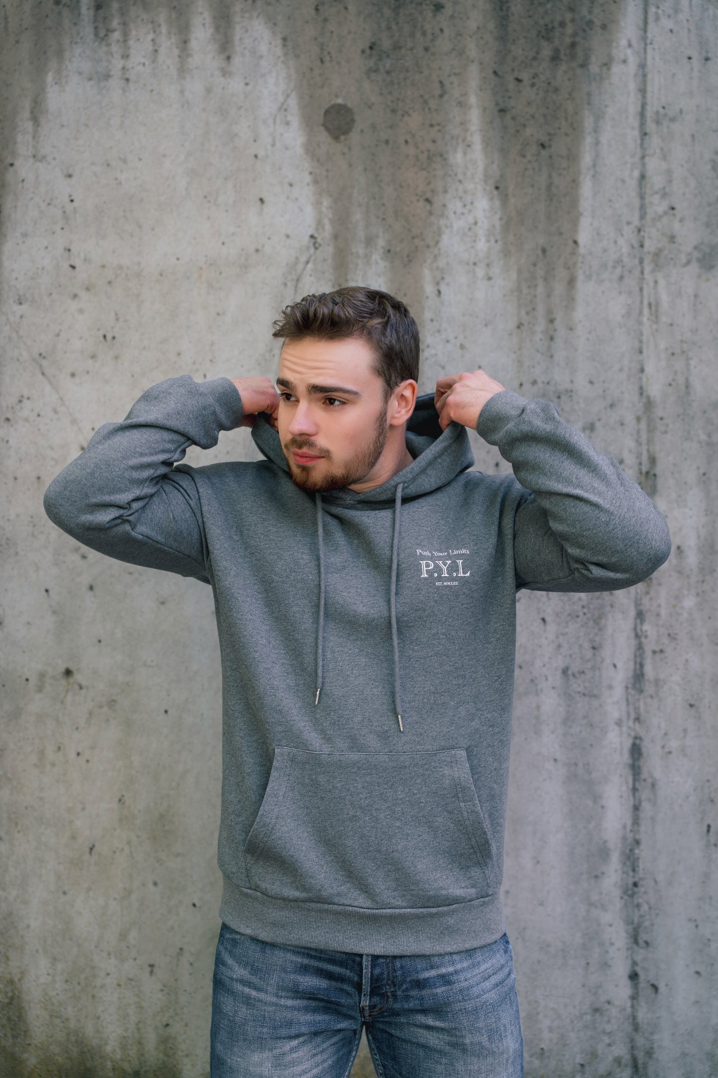 Man wearing a gray hoodie with a logo against a concrete wall