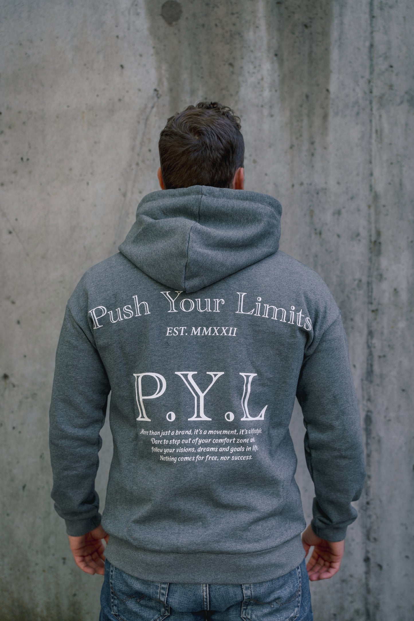 Person wearing a gray hoodie with 'Push Your Limits' text on the back against a concrete wall.
