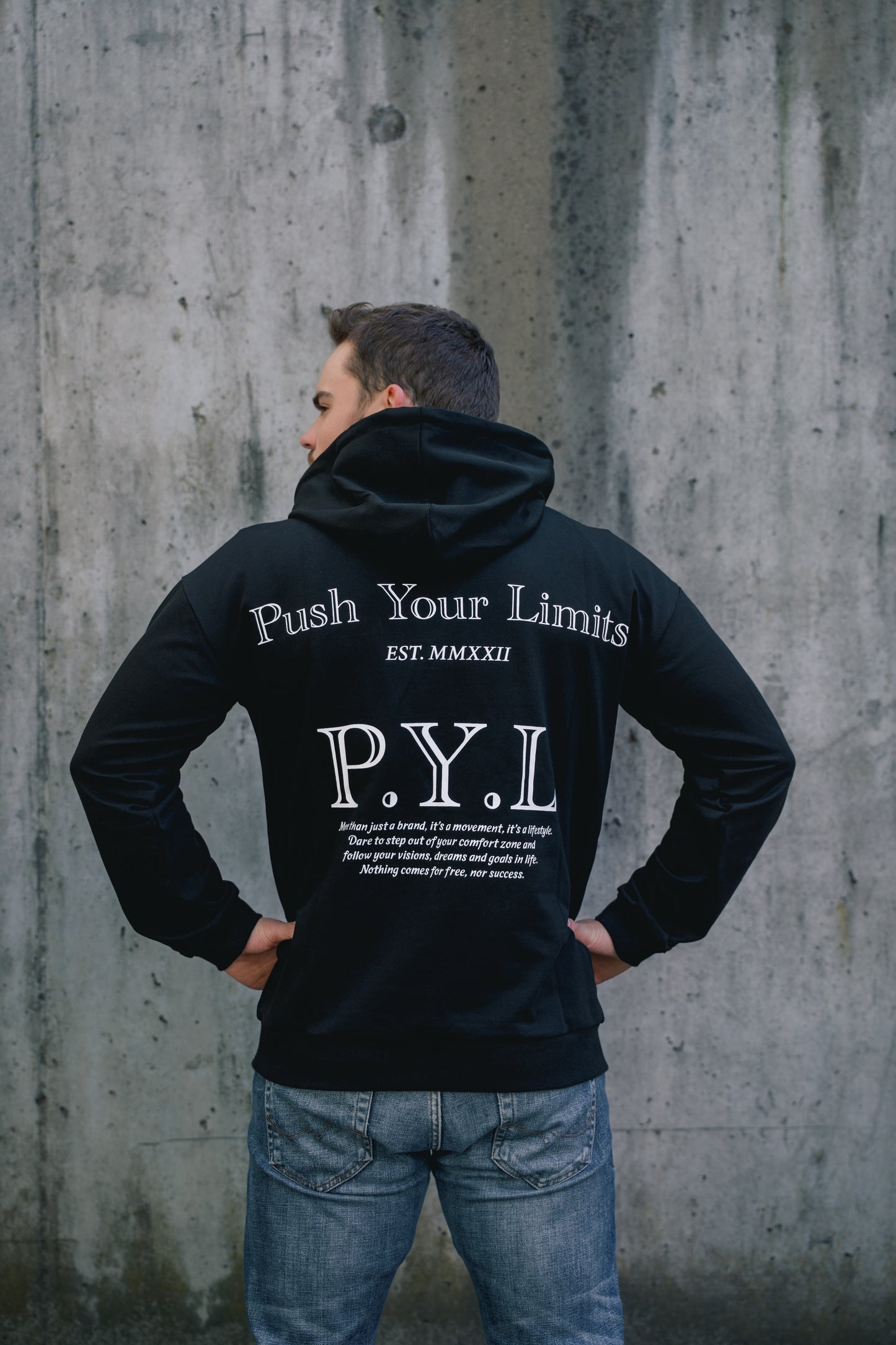 Person wearing a black hoodie with 'Push Your Limits' text, standing against a concrete wall.