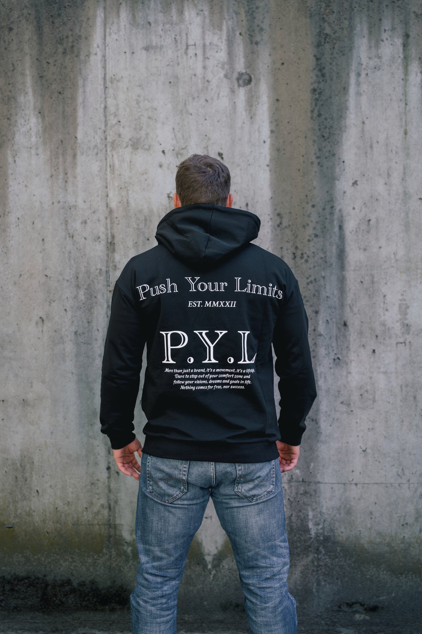 Person wearing a black hoodie with 'Push Your Limits' text against a concrete wall
