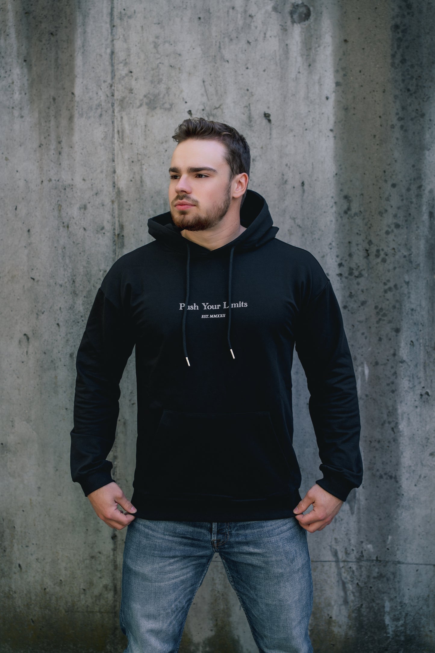 Man wearing a black hoodie with text against a concrete wall