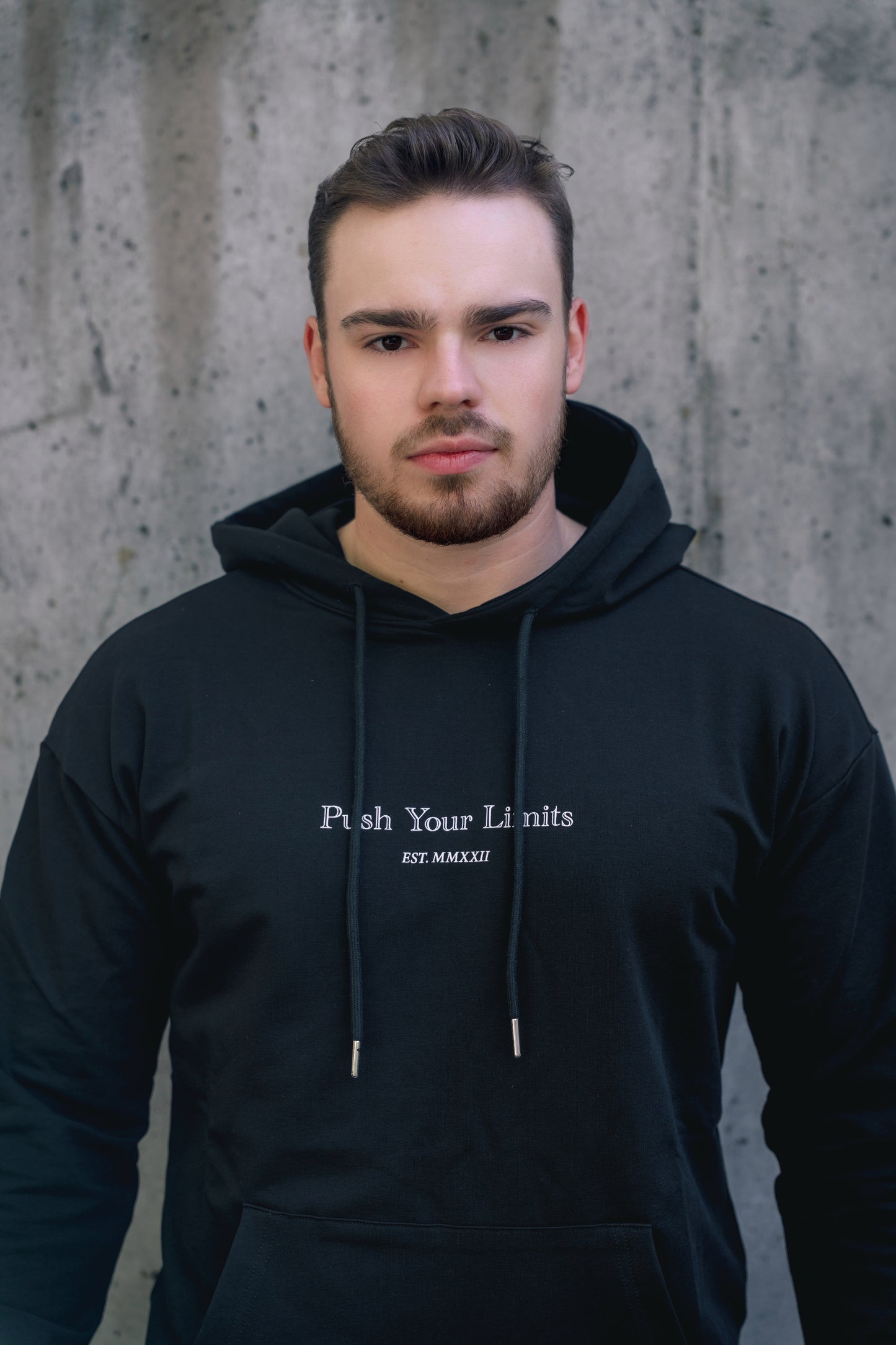 Man wearing a black hoodie with text against a concrete wall