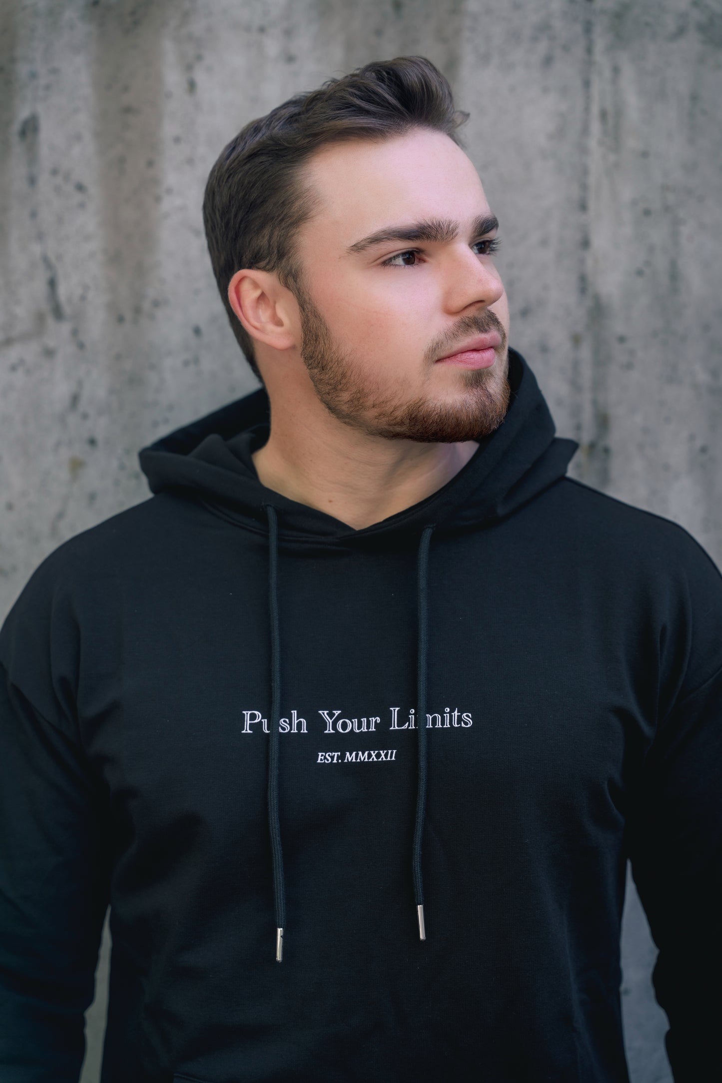 Man wearing a black hoodie with 'Push Your Limits' text against a concrete wall.