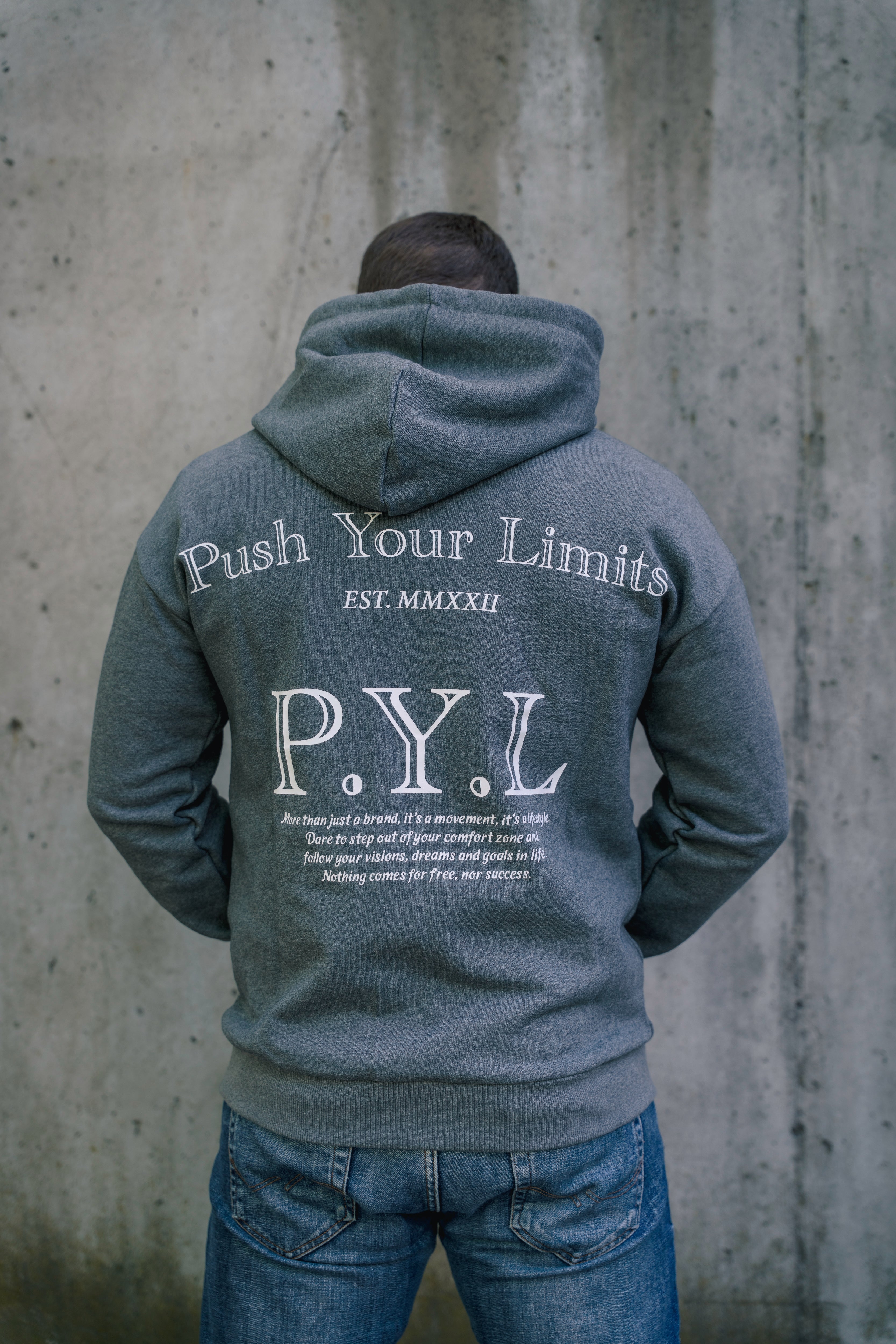 Person wearing a hoodie with 'Push Your Limits' text on the back against a concrete wall.