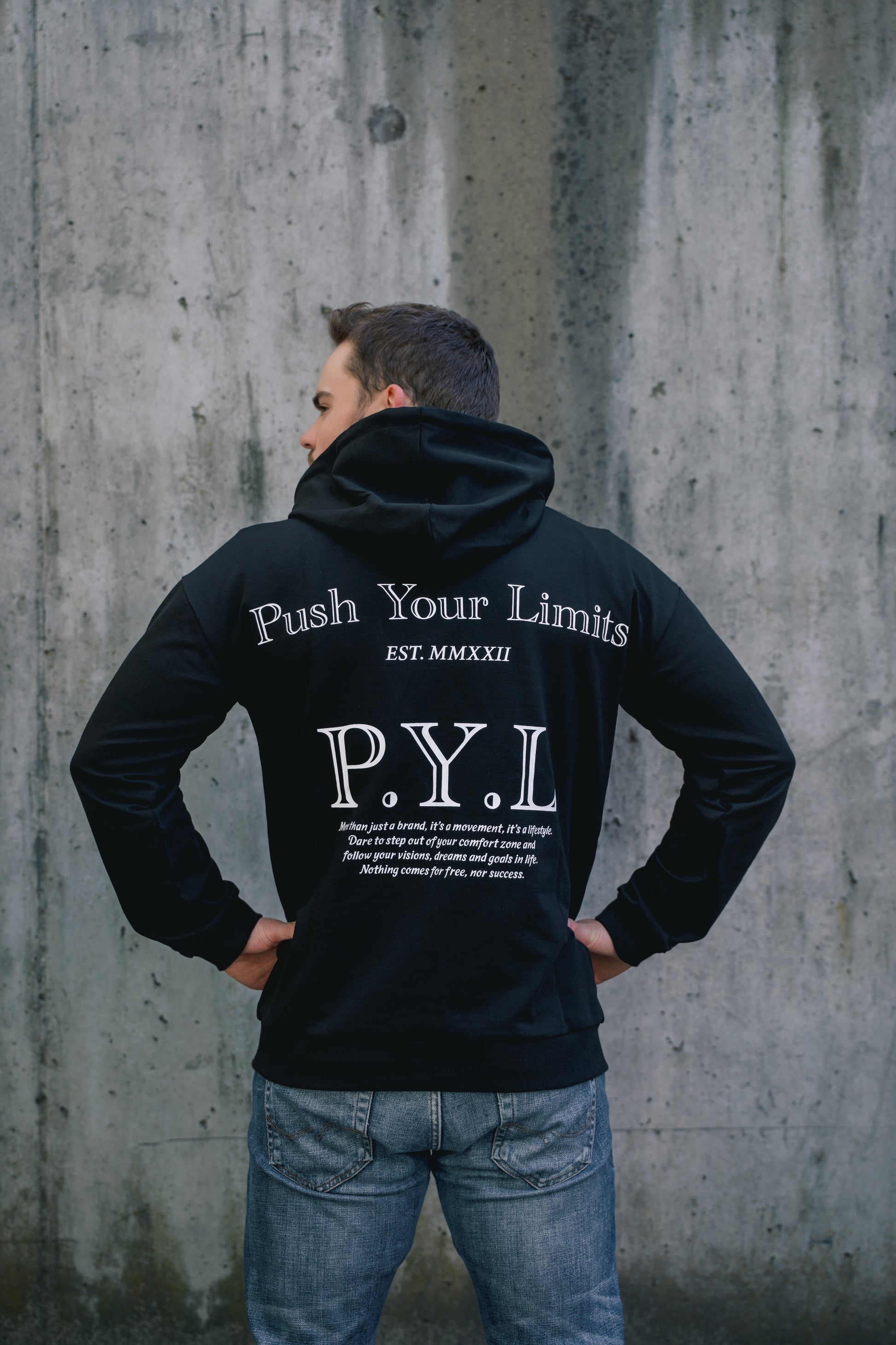 Person wearing a black hoodie with 'Push Your Limits' text, standing against a concrete wall.