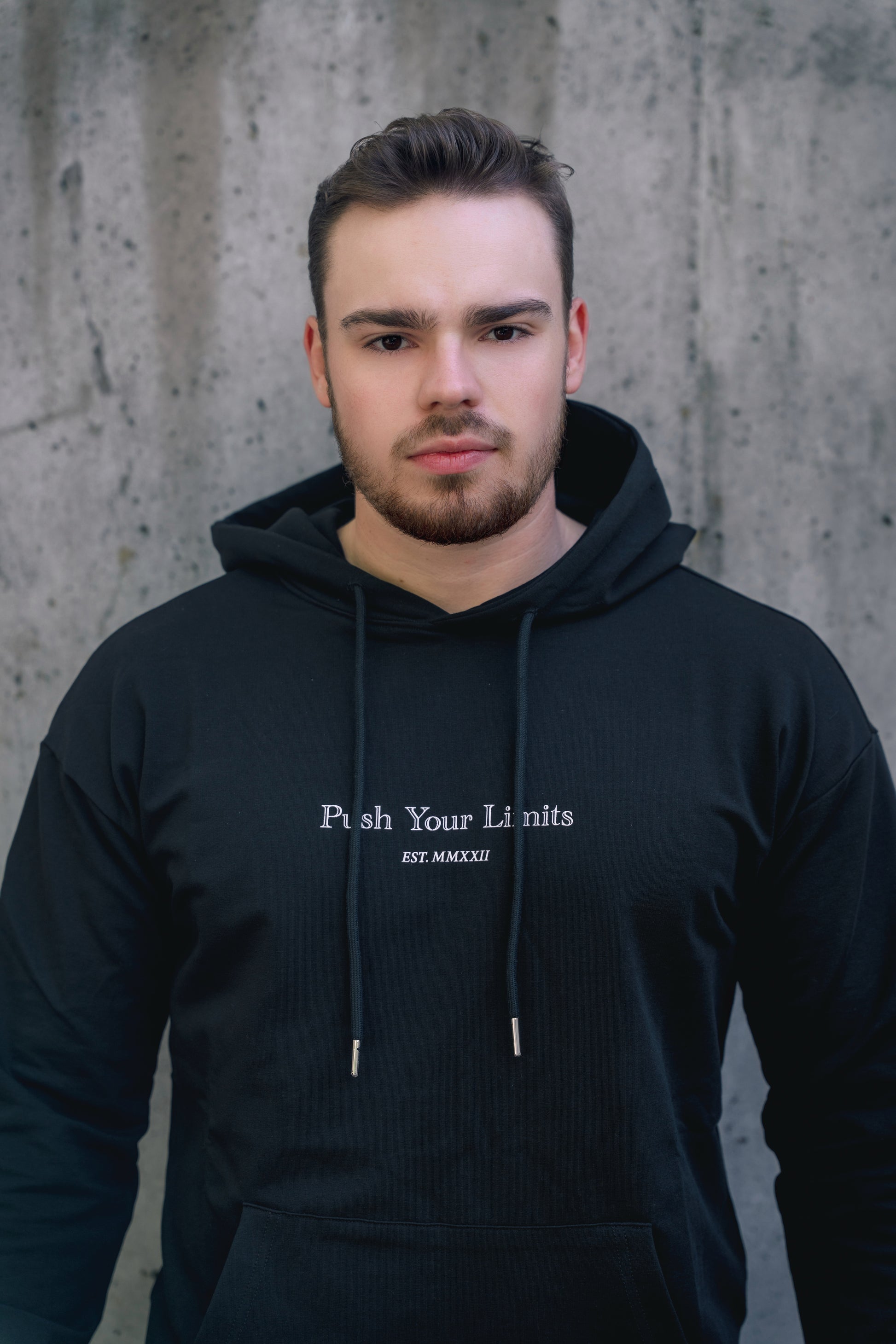 Man wearing a black hoodie with text against a concrete wall